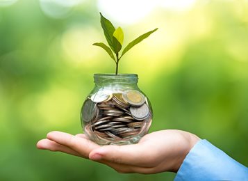 hand holding a jar of money with small plant sprouting out