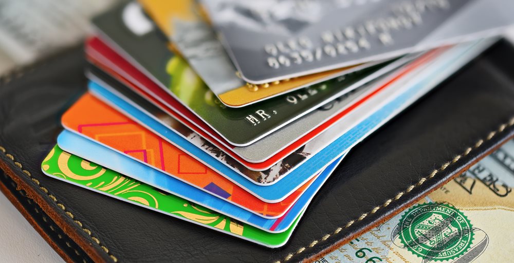 A stack of multi colored debit cards piled on top of a leather wallet