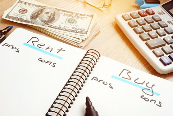 Note book with rent and buy pros and cons listed in it on a desk surrounded by a calculator and money