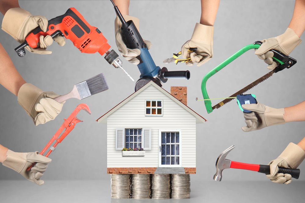 a house surrounded by people's hands holding renovation tools like hammers and saws