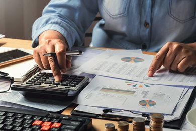 person at desk with calculator, spreadsheet, coins