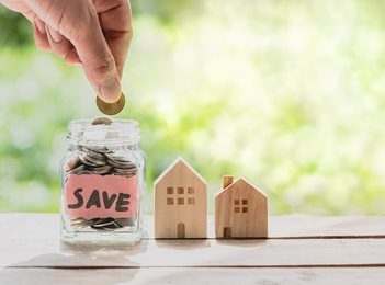 person putting coins into "save" jar with home figurine