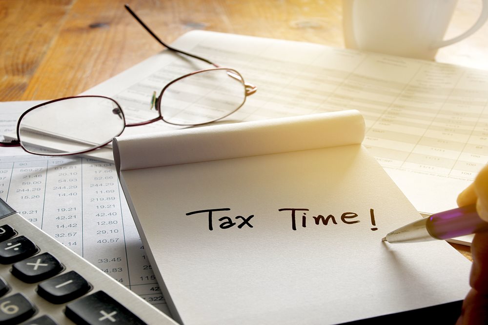 Tax Time written on a note pad, on a desk, surrounded by an income sheet and calculator